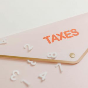A conceptual image of a pink envelope labeled 'Taxes' with scattered numbers, symbolizing tax calculations.