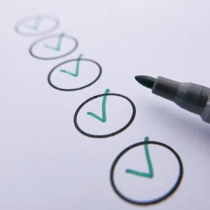 Close-up of a checklist with green checkmarks on white paper using a marker.