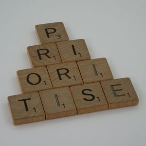 Close-up of wooden Scrabble tiles spelling 'prioritise' on a white surface, set in a pyramid shape.