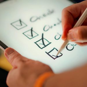 Close-up of a digital checklist being marked off on a tablet with a stylus pen.