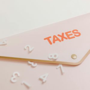 A conceptual image of a pink envelope labeled 'Taxes' with scattered numbers, symbolizing tax calculations.
