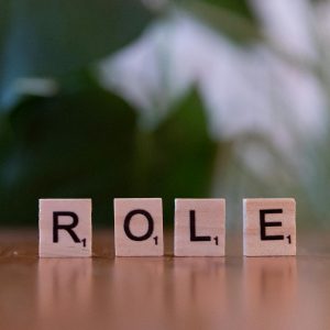 Close-up of Scrabble tiles spelling 'ROLE' on a wooden surface with a blurred background.